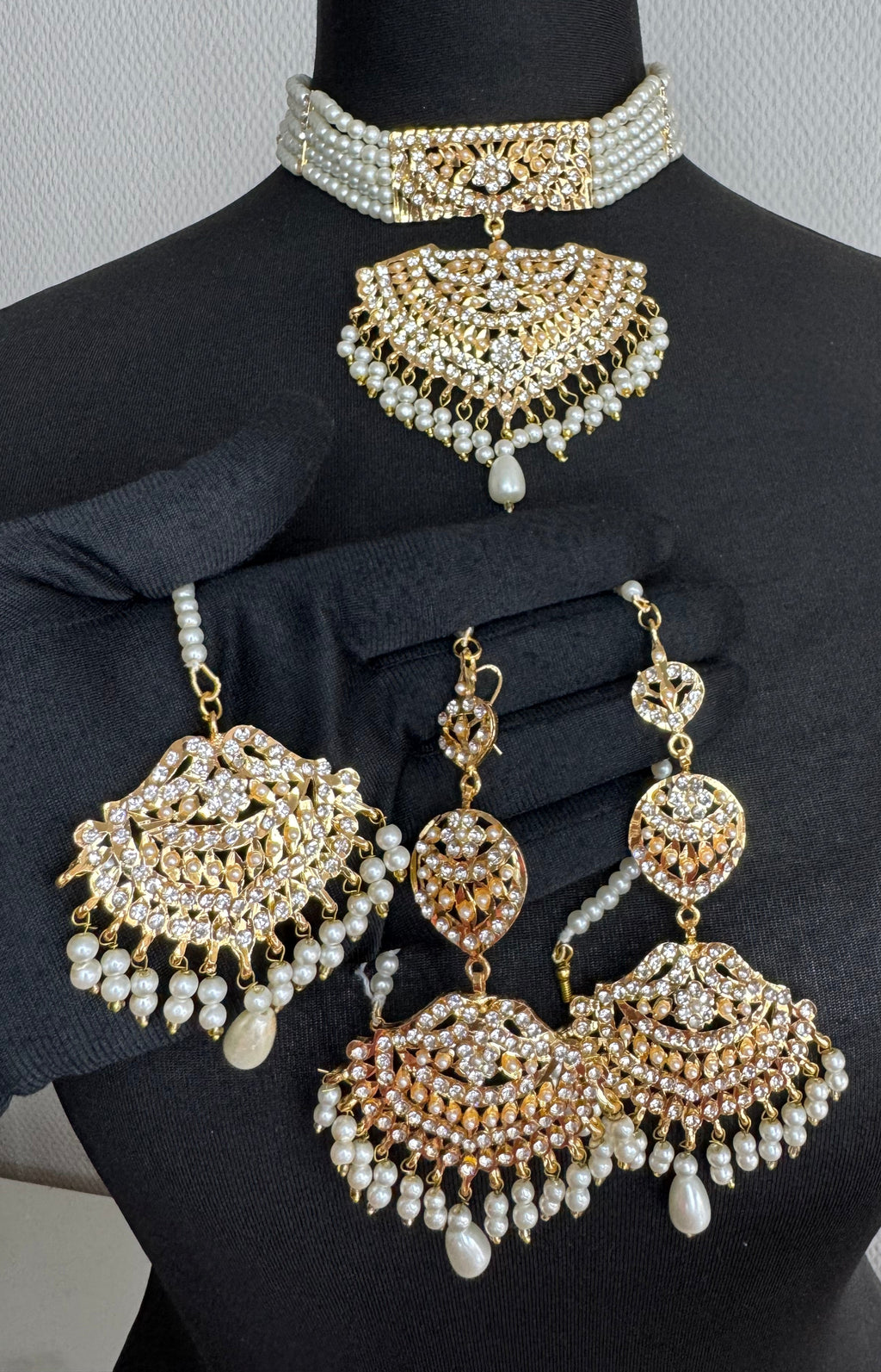 Pair of gold and pearl beaded bracelets on a black mannequin arm against a neutral background